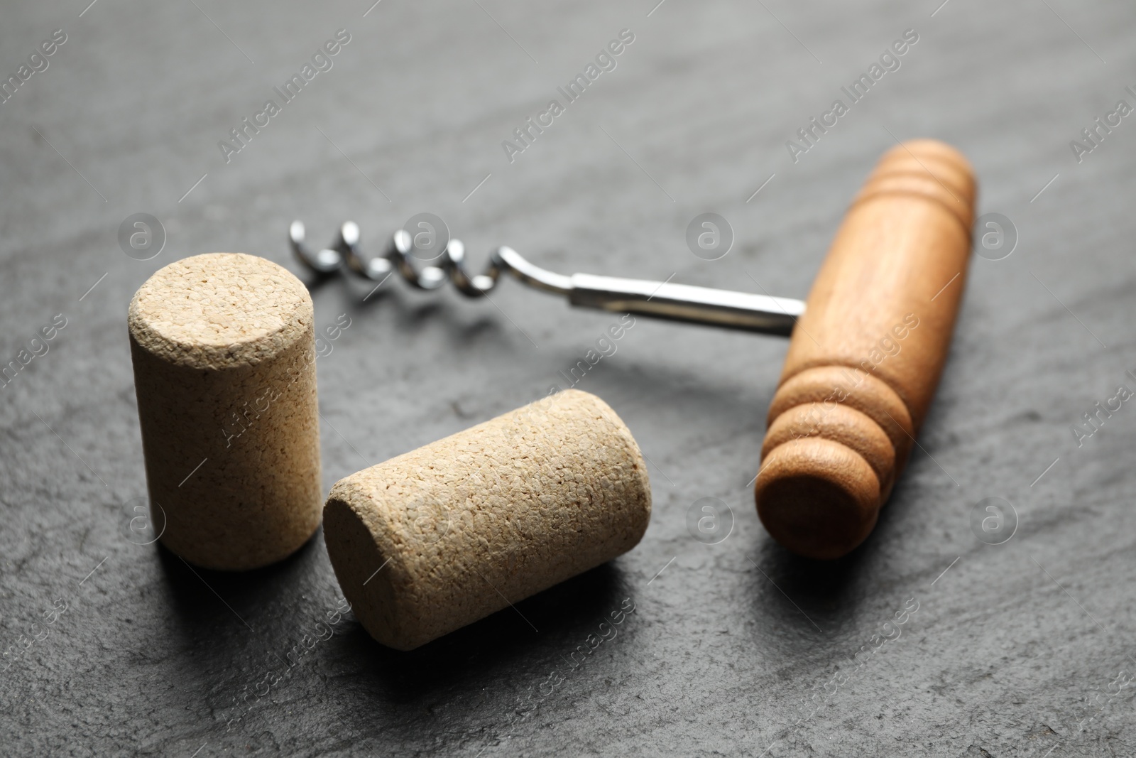 Photo of Corkscrew with wooden handle and corks on black table, closeup