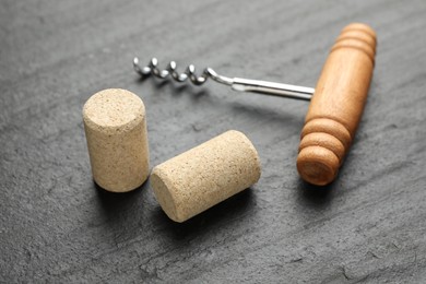 Corkscrew with wooden handle and corks on black table, closeup