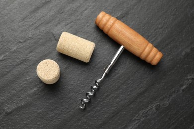 Corkscrew with wooden handle and corks on black table, top view