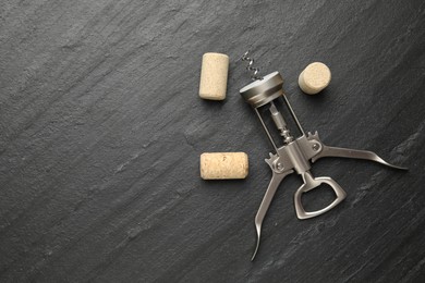 Wing corkscrew and corks on black table, top view. Space for text