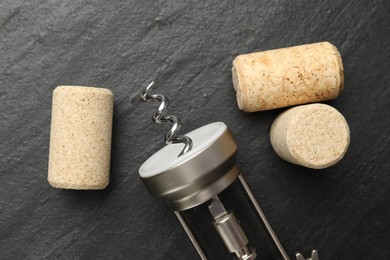 Wing corkscrew and corks on black table, top view