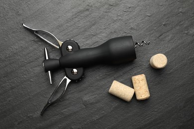 Wing corkscrew and corks on black table, top view