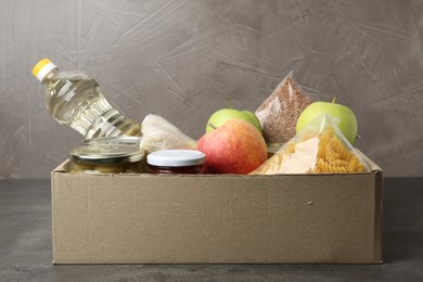 Photo of Different food products for donation in box on grey table