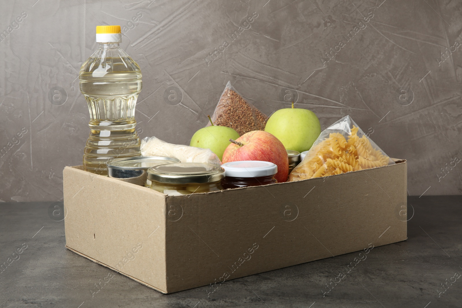 Photo of Different food products for donation in box on grey table