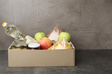 Photo of Different food products for donation in box on grey table, space for text