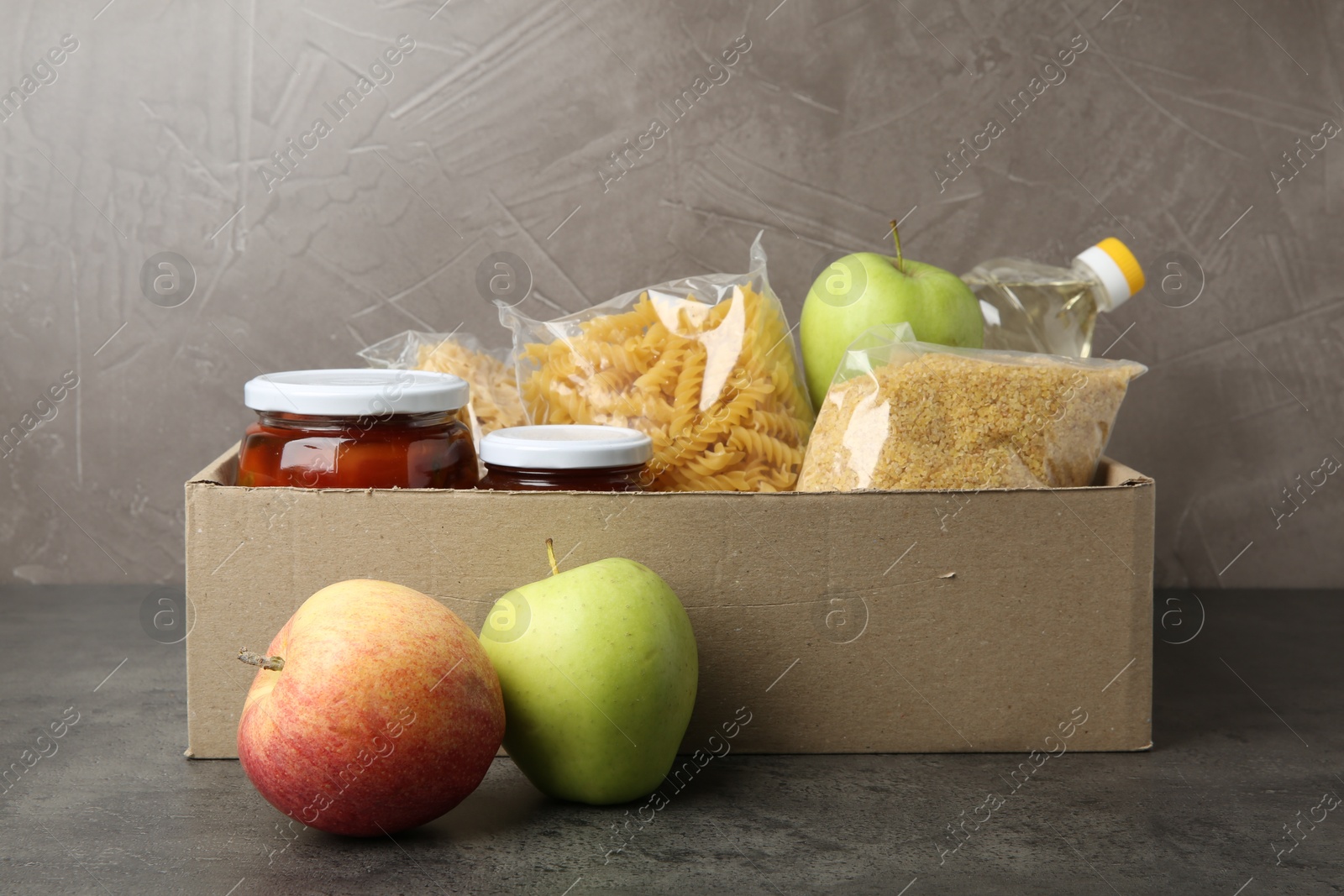 Photo of Different food products for donation in box on grey table