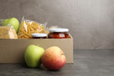 Photo of Different food products for donation in box on grey table, space for text