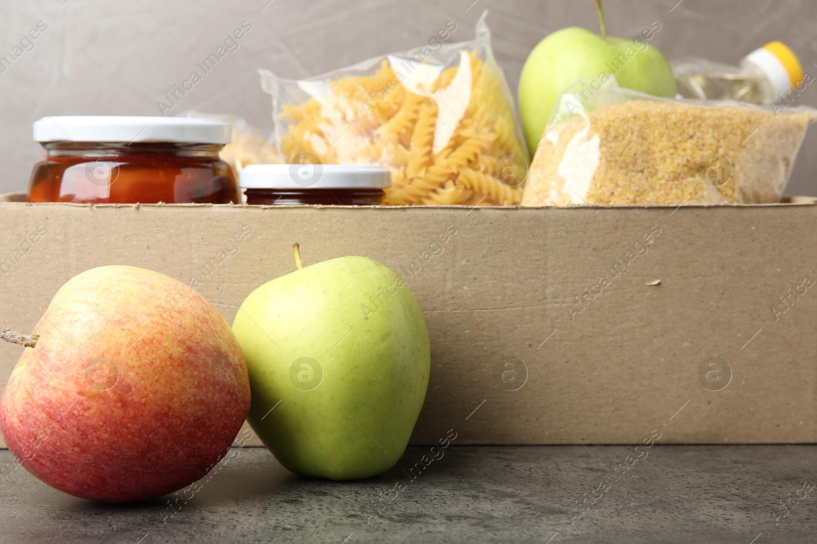 Photo of Different food products for donation in box on grey table, closeup