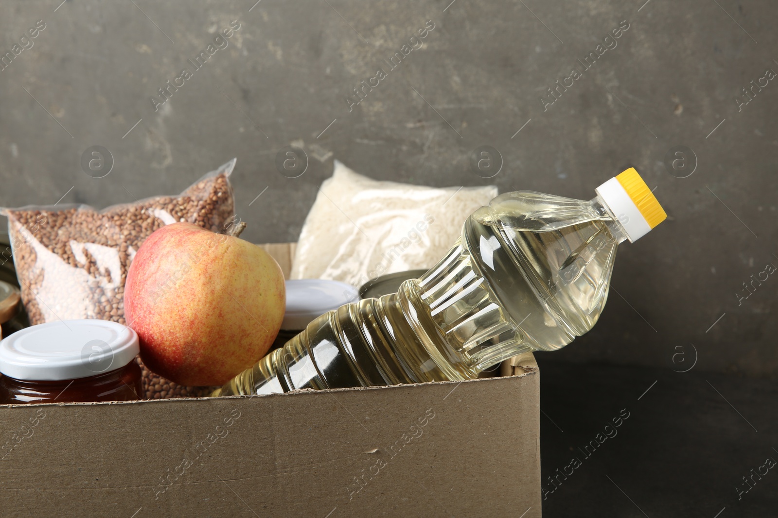 Photo of Different food products for donation in box on grey table, closeup