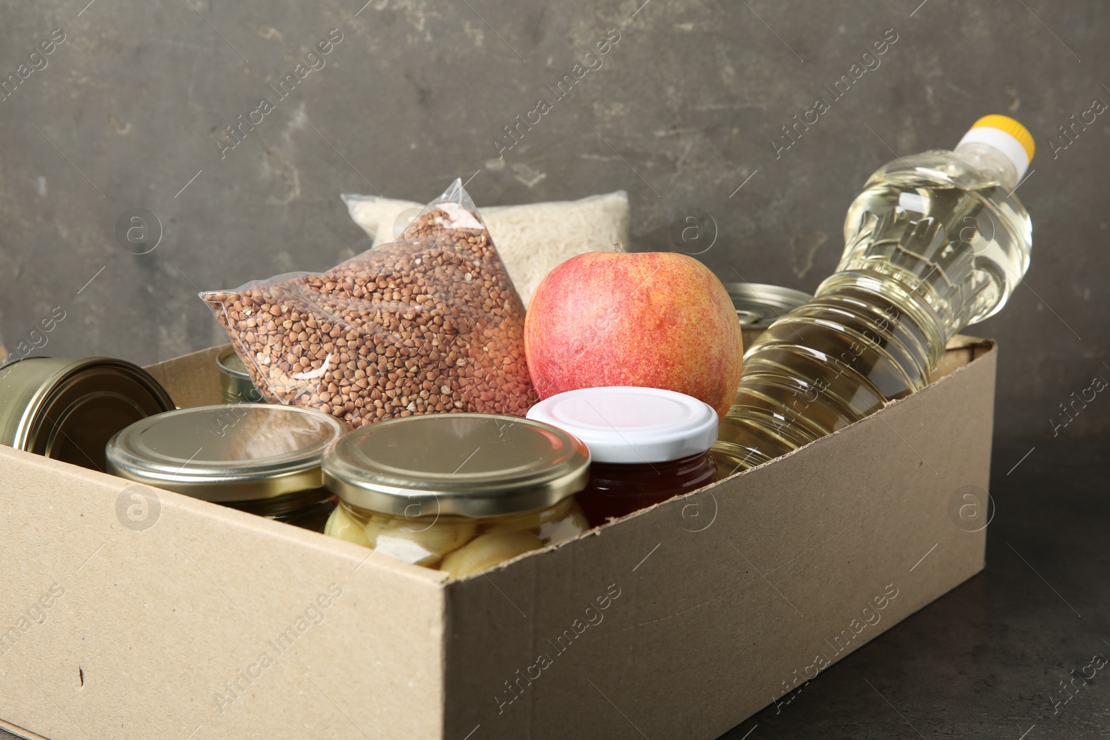 Photo of Different food products for donation in box on grey table, closeup