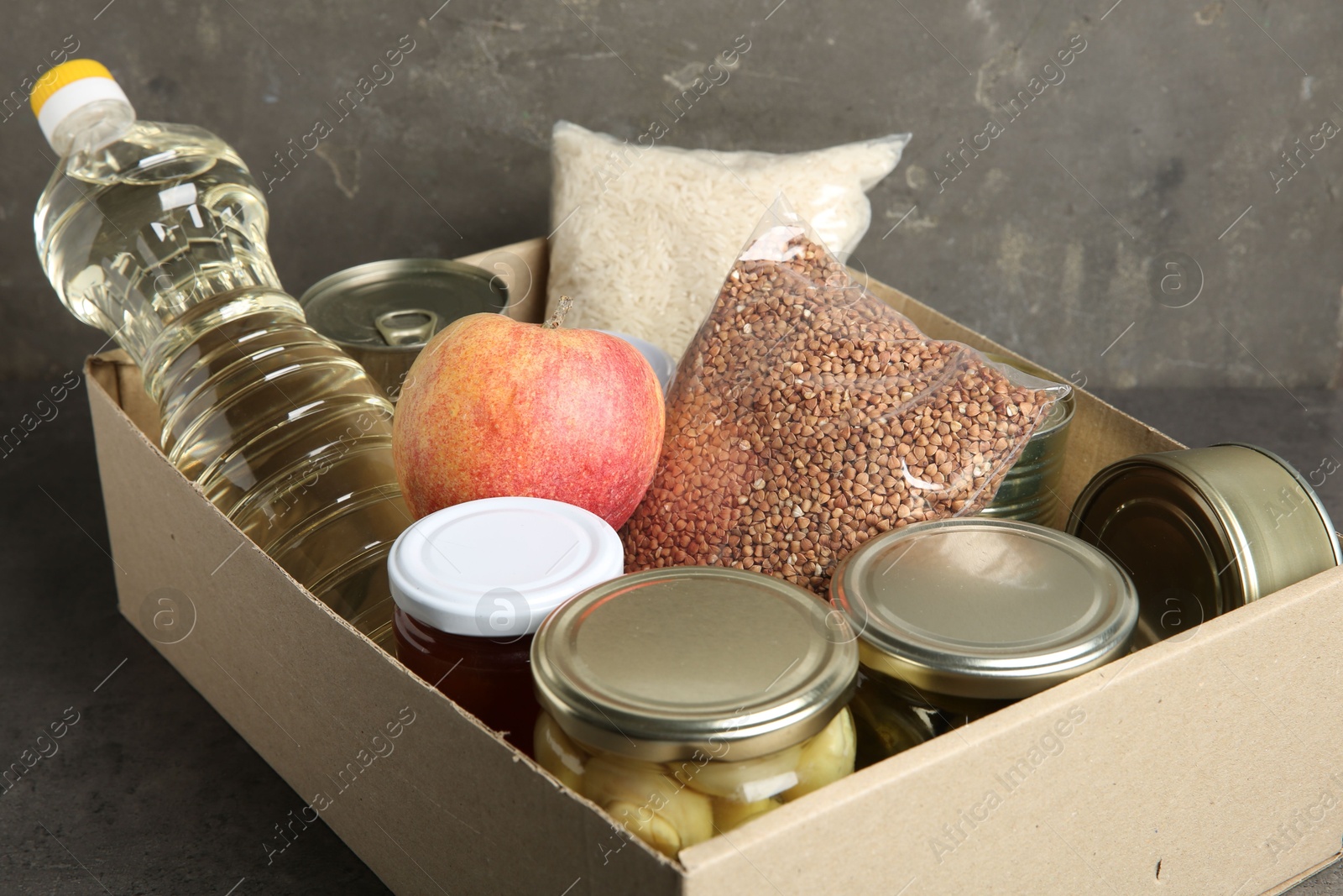 Photo of Different food products for donation in box on grey table, closeup