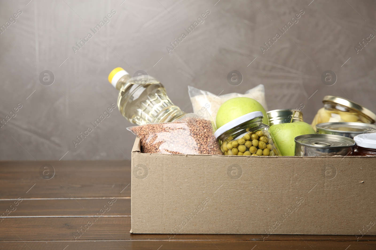 Photo of Different food products for donation in box on wooden table, space for text