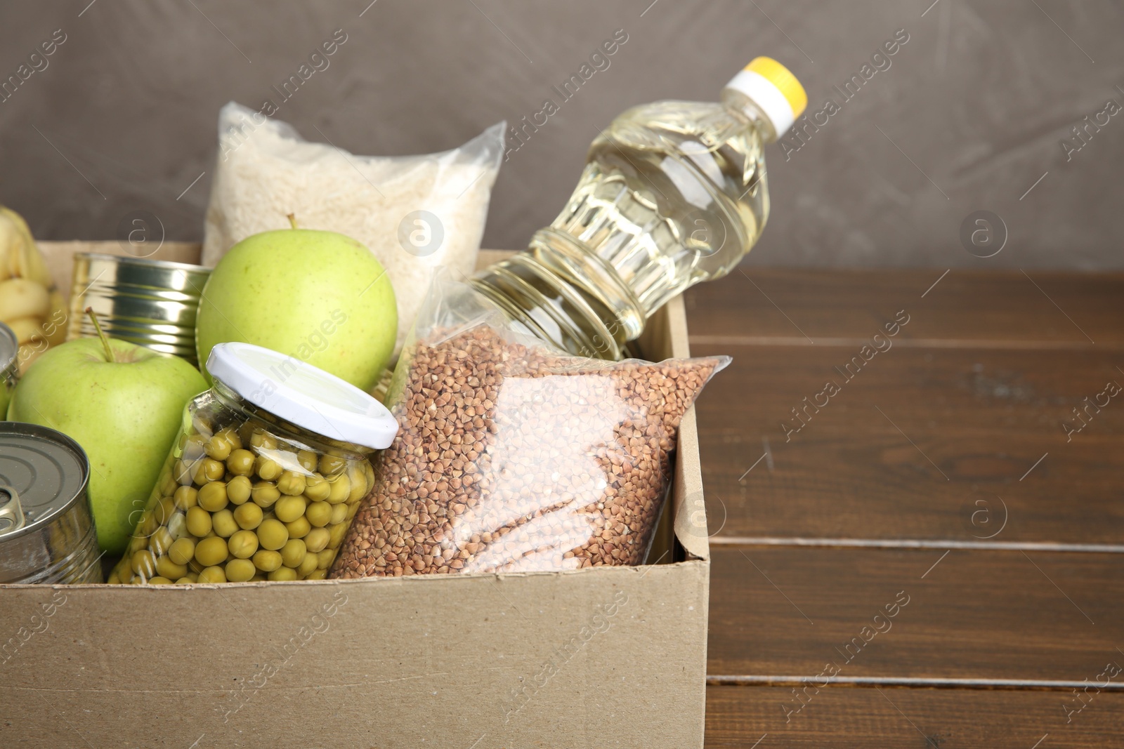 Photo of Different food products for donation in box on wooden table, closeup. Space for text