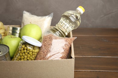 Photo of Different food products for donation in box on wooden table, closeup. Space for text