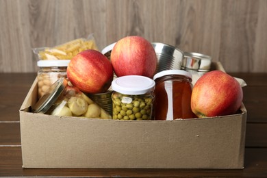 Photo of Different food products for donation in box on wooden table