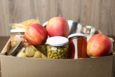 Photo of Different food products for donation in box on table, closeup