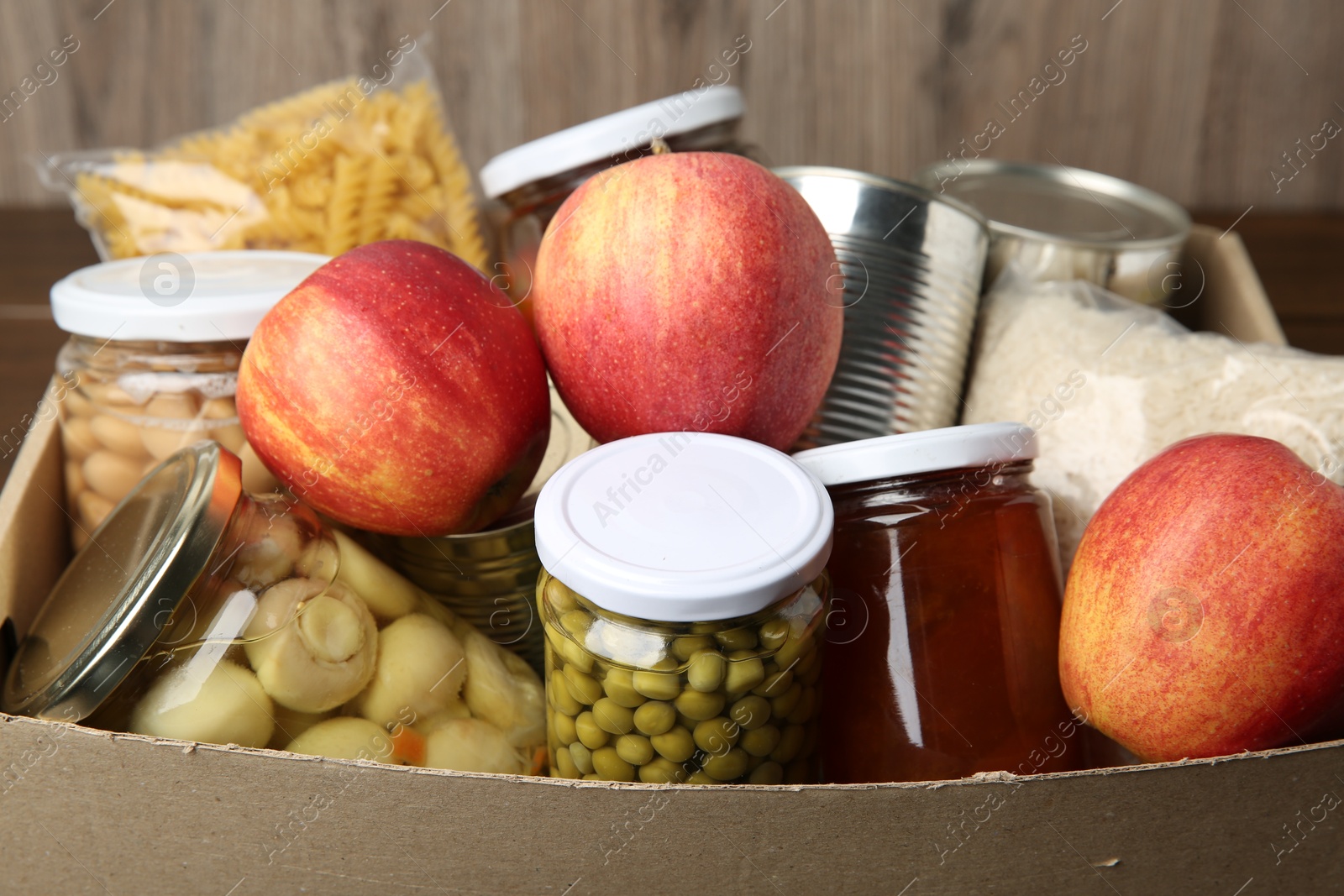 Photo of Different food products for donation in box on table, closeup