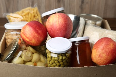 Photo of Different food products for donation in box on table, closeup