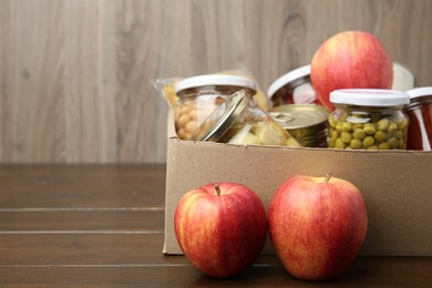 Photo of Different food products for donation in box on wooden table, space for text