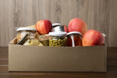 Photo of Different food products for donation in box on wooden table