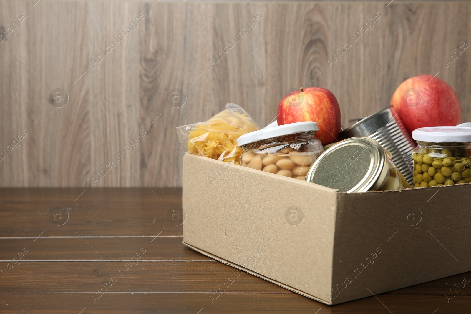 Photo of Different food products for donation in box on wooden table, space for text