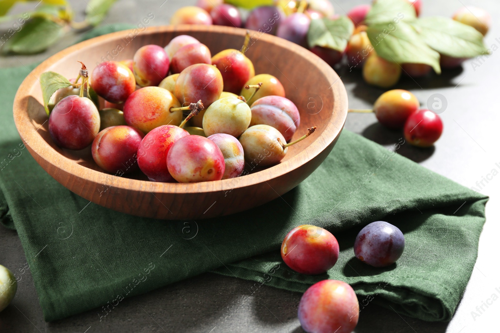 Photo of Ripe plums in bowl on grey table, closeup