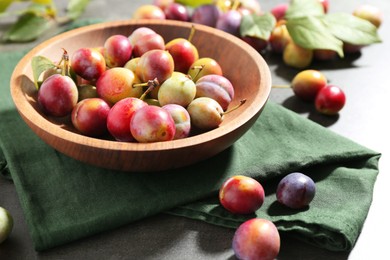 Photo of Ripe plums in bowl on grey table, closeup