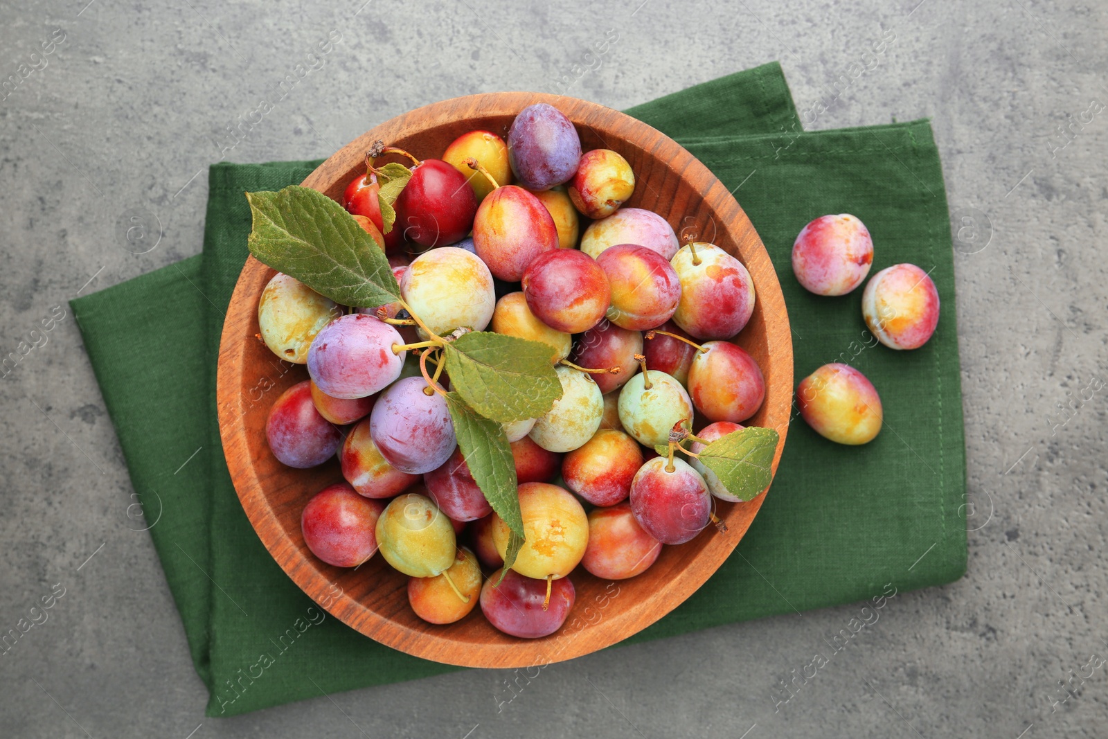 Photo of Ripe plums in bowl on grey textured table, flat lay