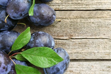 Photo of Tasty ripe plums and leaves on wooden table, flat lay. Space for text