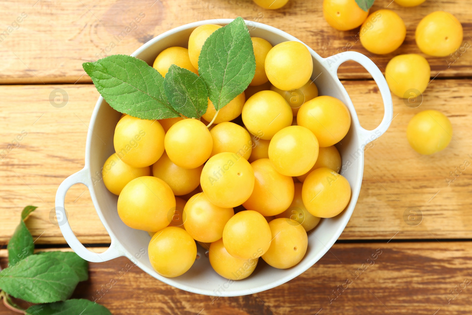 Photo of Tasty ripe plums and leaves in colander on wooden table, flat lay