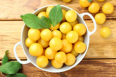 Photo of Tasty ripe plums and leaves in colander on wooden table, flat lay