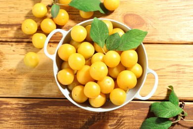 Photo of Tasty ripe plums and leaves in colander on wooden table, flat lay