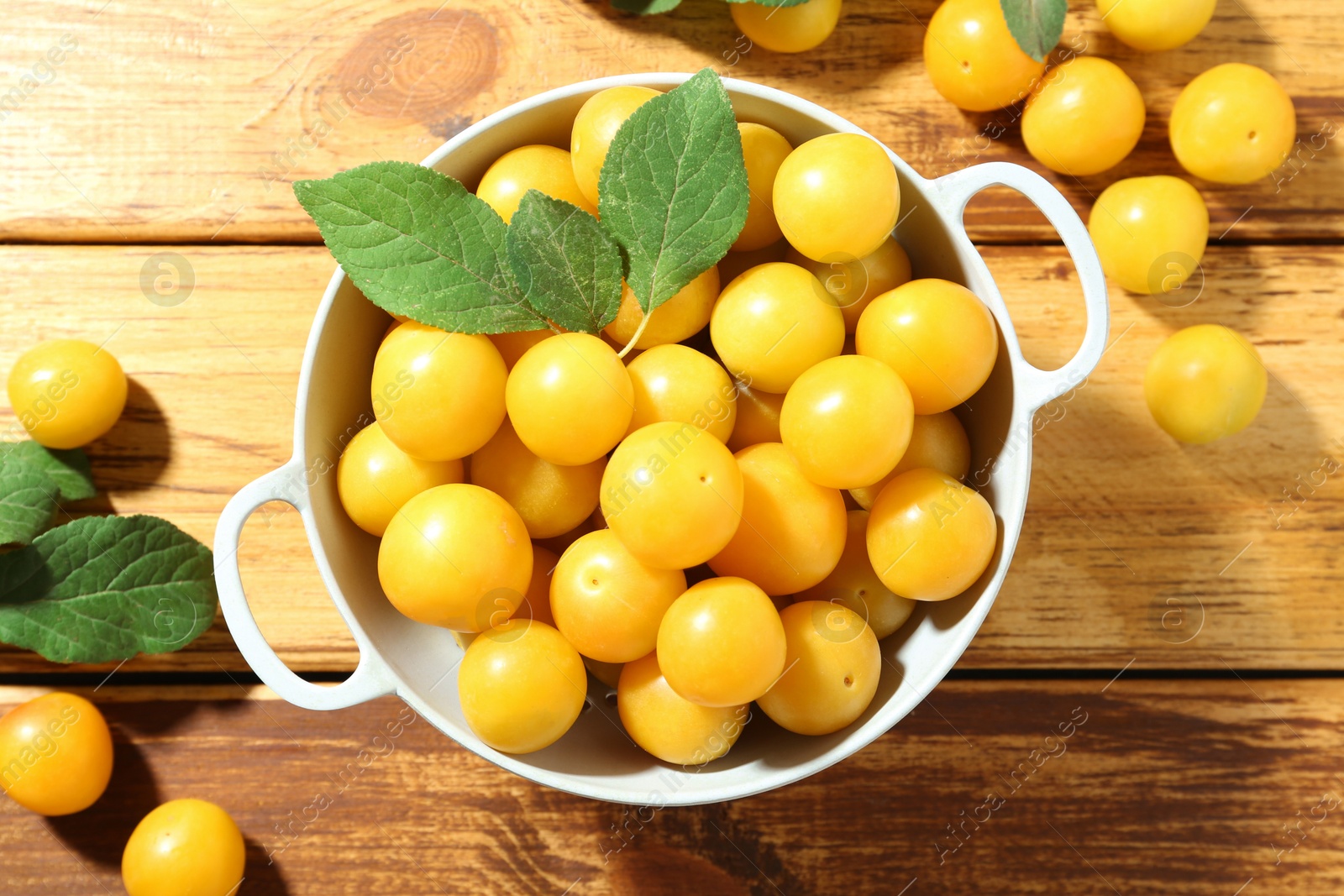 Photo of Tasty ripe plums and leaves in colander on wooden table, flat lay