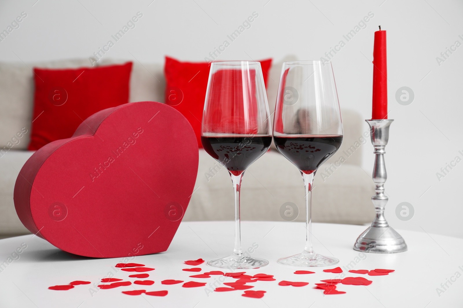 Photo of Burning candle, wine in glasses and paper hearts on table indoors