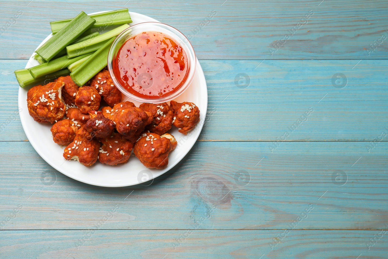 Photo of Tasty cauliflower buffalo wings, sauce and celery on light blue wooden table, top view. Space for text