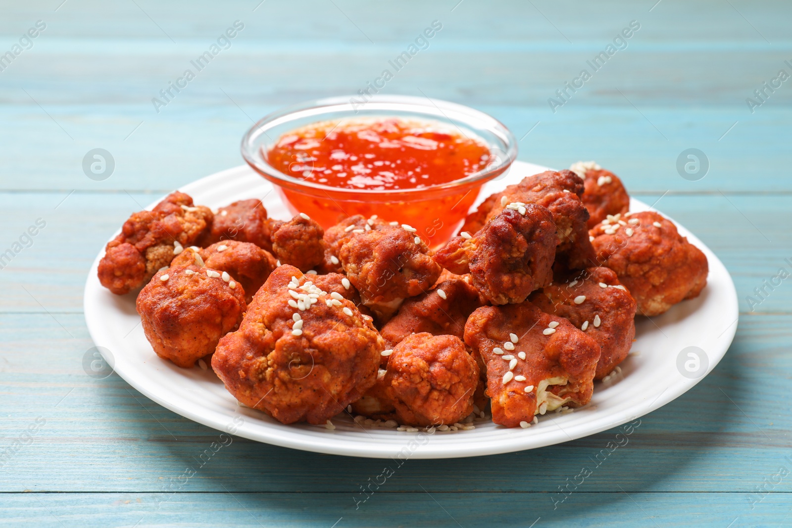 Photo of Tasty cauliflower buffalo wings and sauce on light blue wooden table, closeup