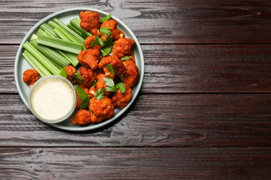 Photo of Tasty cauliflower buffalo wings, sauce and celery on wooden table, top view