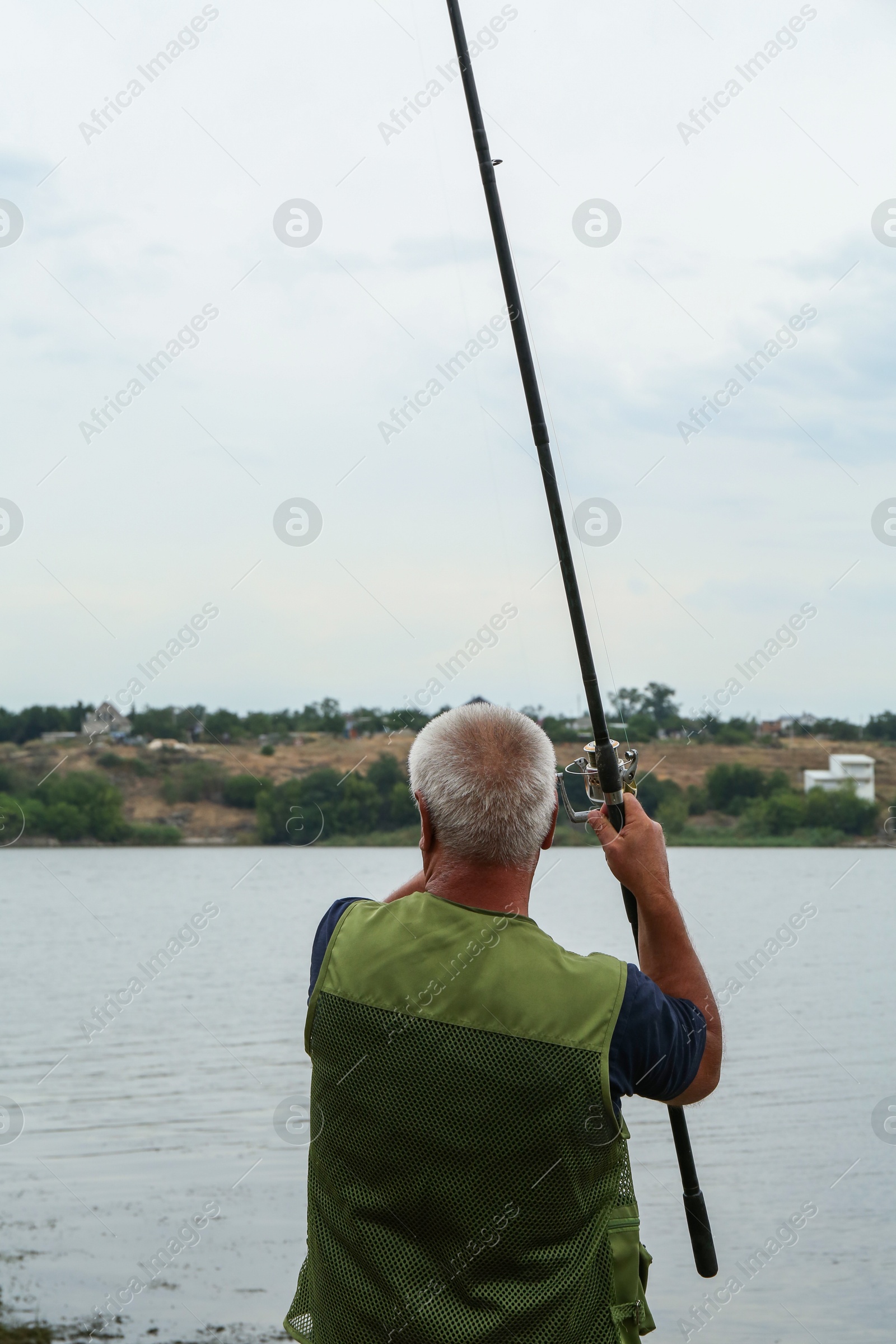 Photo of Fisherman with rod fishing near lake at summer, back view