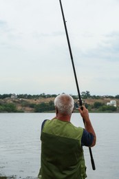 Photo of Fisherman with rod fishing near lake at summer, back view