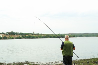 Photo of Fisherman with rod fishing near lake at summer, back view