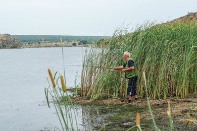 Photo of Fisherman with rod fishing near lake at summer