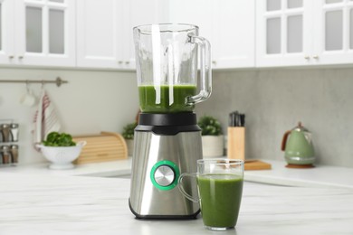 Photo of Modern blender with smoothie and ingredients on white marble table in kitchen