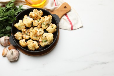 Photo of Tasty baked cauliflower in baking pan, garlic and parsley on white marble table, flat lay. Space for text