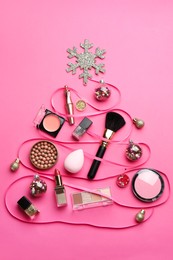 Photo of Christmas tree made of decorative cosmetic products and festive decor on pink background, flat lay