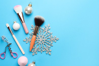 Makeup brushes, eyelash curler and Christmas decor on light blue background, flat lay. Space for text