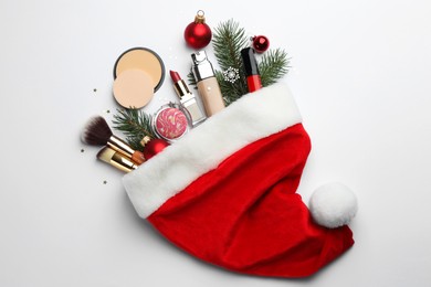 Santa hat with different decorative cosmetic products and Christmas decor on white background, top view