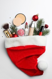 Santa hat with different decorative cosmetic products and Christmas decor on white background, top view