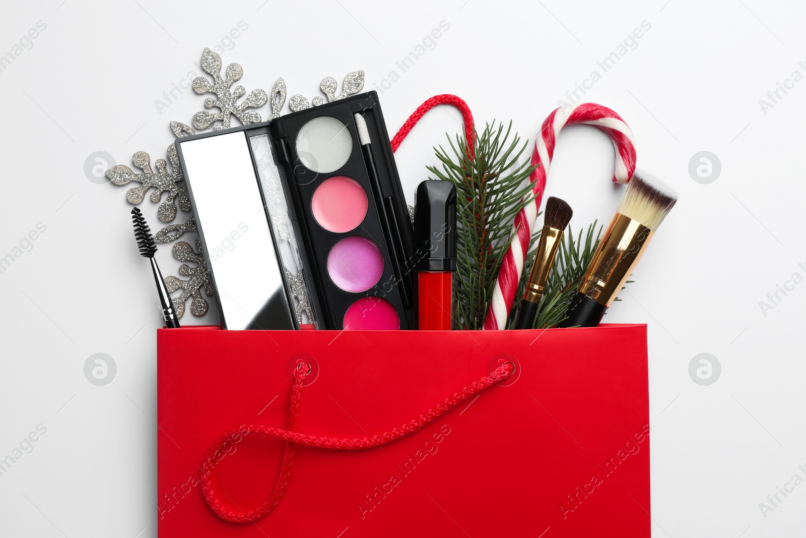 Photo of Different decorative cosmetic products in gift bag and Christmas decor on white background, top view