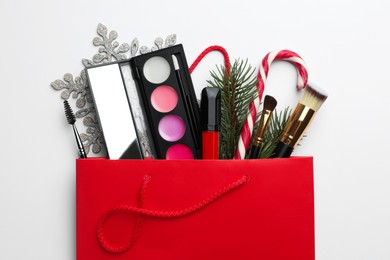 Photo of Different decorative cosmetic products in gift bag and Christmas decor on white background, top view