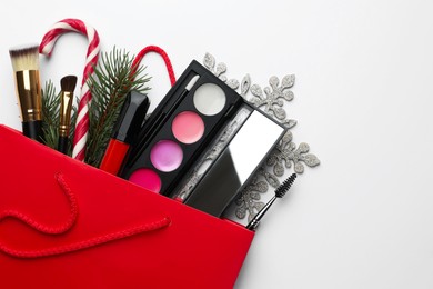 Photo of Different decorative cosmetic products in gift bag and Christmas decor on white background, top view